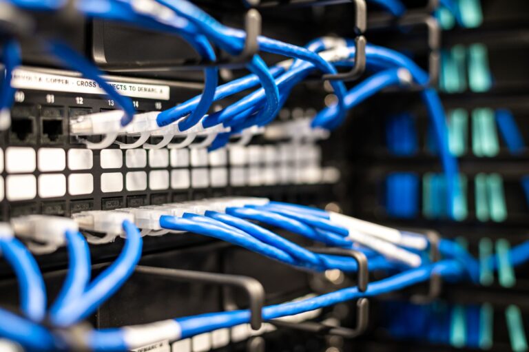 Vista detalhada de cabos de rede azuis conectados a um painel de conexão em um data center.
