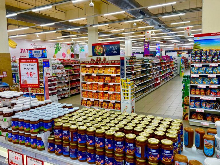 Vista ampla de um corredor de supermercado totalmente abastecido com potes e diversos produtos nas prateleiras.